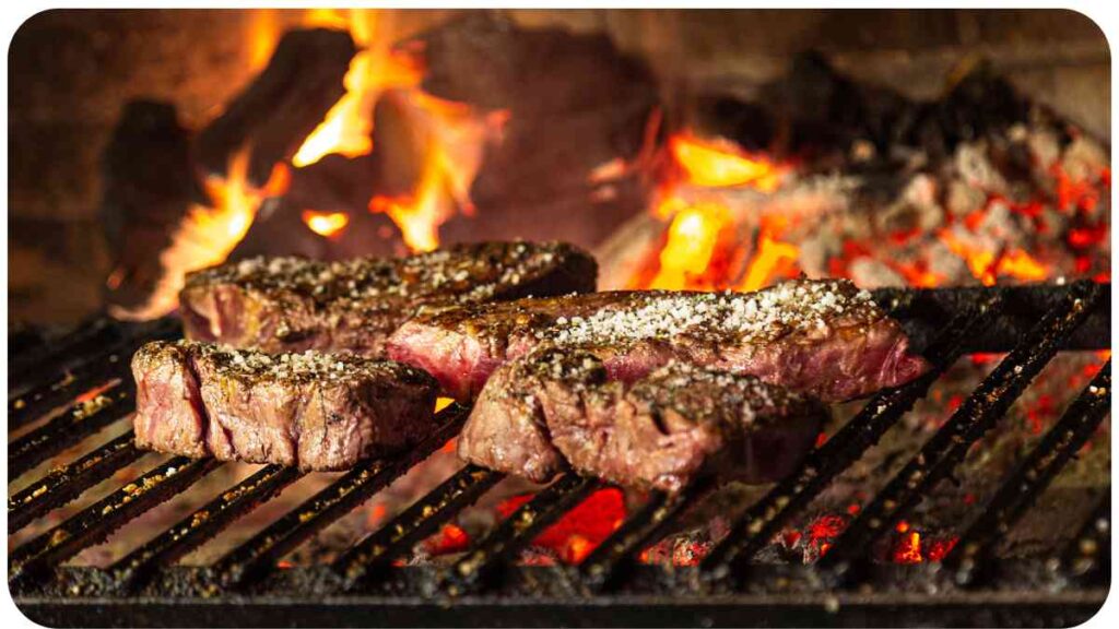 two steaks cooking on a grill in front of a fireplace