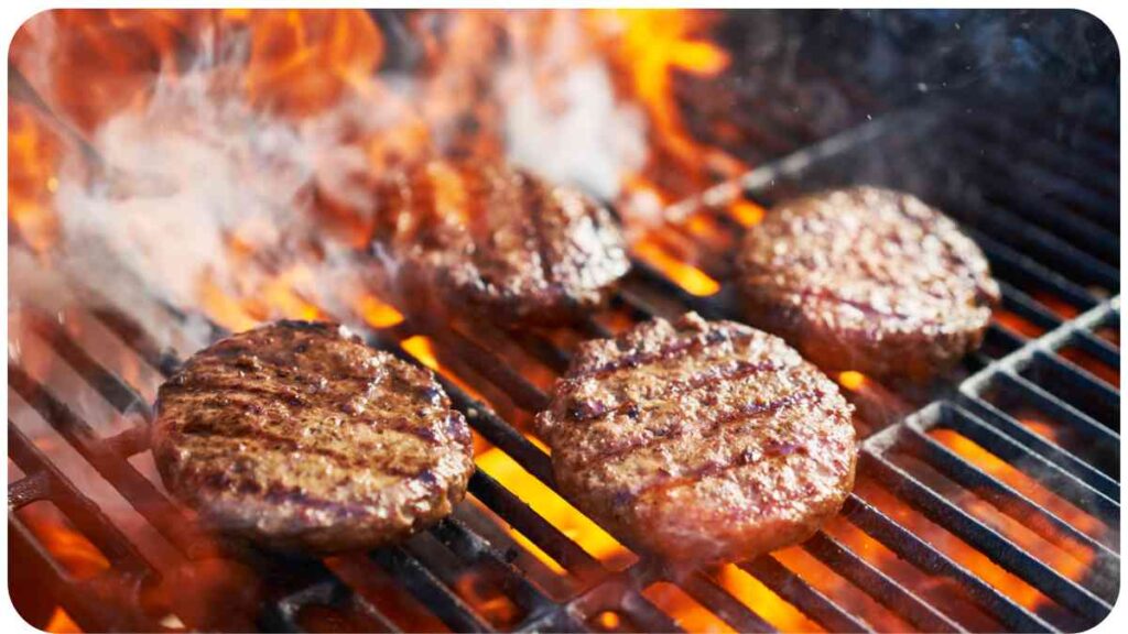 three hamburgers are cooking on an outdoor grill